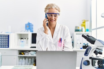 Middle age blonde woman wearing scientist uniform talking on the smartphone working at laboratory