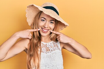 Young caucasian woman wearing summer hat smiling cheerful showing and pointing with fingers teeth and mouth. dental health concept.