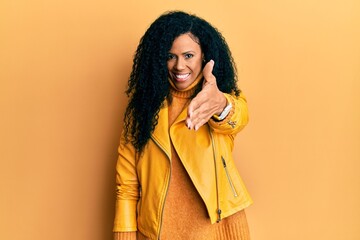 Middle age african american woman wearing wool winter sweater and leather jacket smiling friendly offering handshake as greeting and welcoming. successful business.