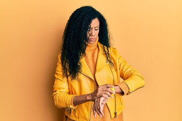 Middle age african american woman wearing wool winter sweater and leather jacket checking the time on wrist watch, relaxed and confident