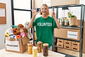 Young caucasian woman wearing volunteer t shirt at donations stand showing and pointing up with...