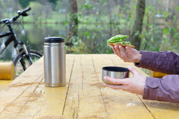 Female hands are holding a sandwich with herbs. Snack in nature by the forest lake, bike ride.