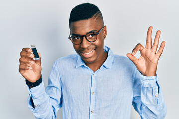 Young african american man holding removable memory usb doing ok sign with fingers, smiling friendly gesturing excellent symbol