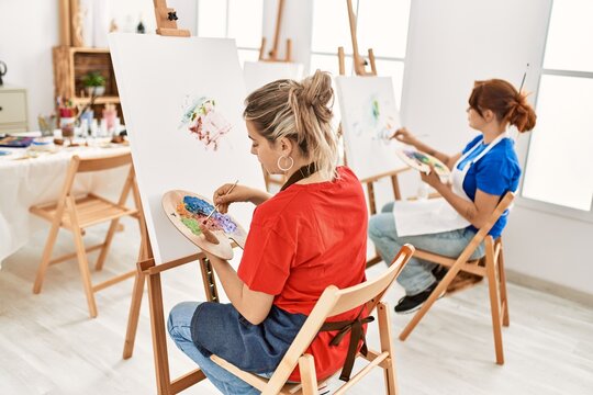 Two artist student women on back view painting at art school.