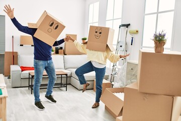 Middle age hispanic couple playing and dancing with funny cardboard boxes at new home.