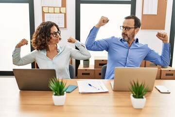 Middle age hispanic woman and man sitting with laptop at the office showing arms muscles smiling proud. fitness concept.