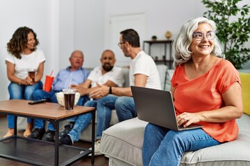 Group of middle age friends sitting on the sofa speaking. Woman smiling happy using laptop at home.