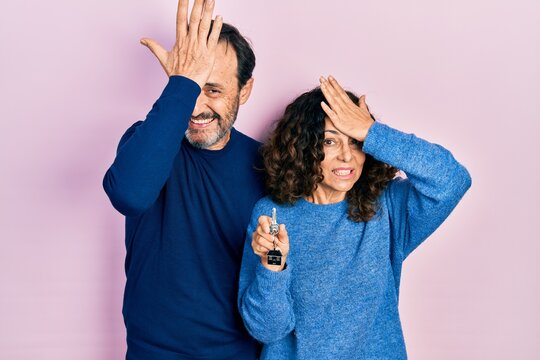 Middle age couple of hispanic woman and man holding keys of new home surprised with hand on head for mistake, remember error. forgot, bad memory concept.