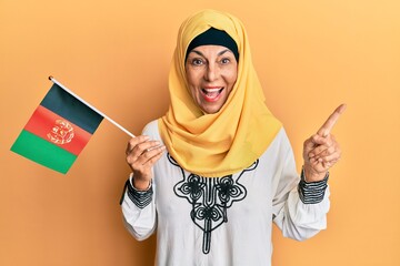 Middle age hispanic woman holding afghanistan flag smiling happy pointing with hand and finger to...