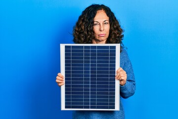 Middle age hispanic woman holding photovoltaic solar panel skeptic and nervous, frowning upset because of problem. negative person.