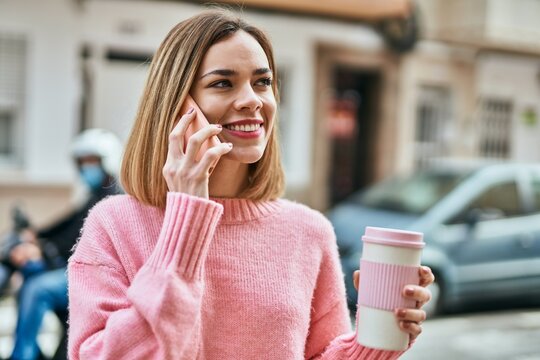 Young caucasian girl talking on the smartphone and drinking coffee at the city.