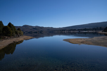 The pure water lake, forest and mountains in a sunny day. The trees, hills and blue sky reflection in the water surface. 