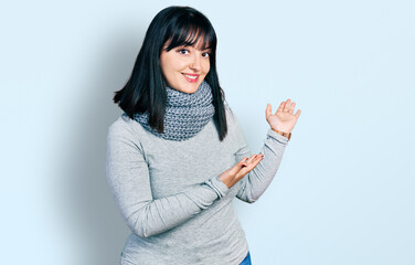 Young hispanic plus size woman wearing winter scarf inviting to enter smiling natural with open hand