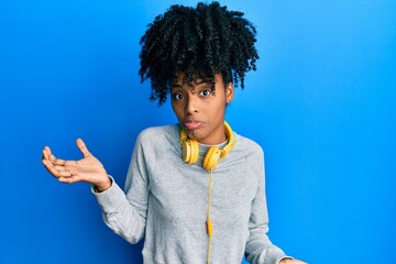 African american woman with afro hair wearing sweatshirt and using headphones clueless and confused...