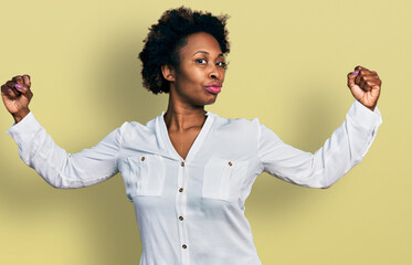 African american woman with afro hair wearing casual white t shirt showing arms muscles smiling proud. fitness concept.