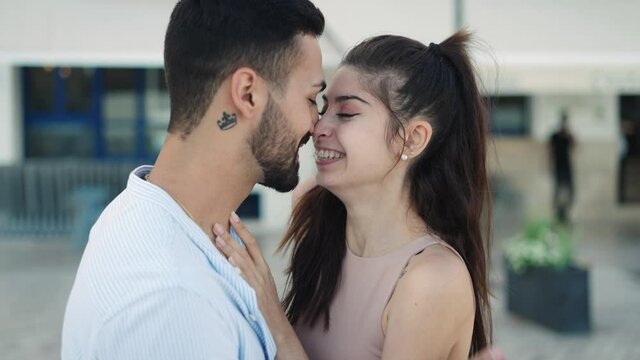 Smiling Hispanic couple talking and kissing on street