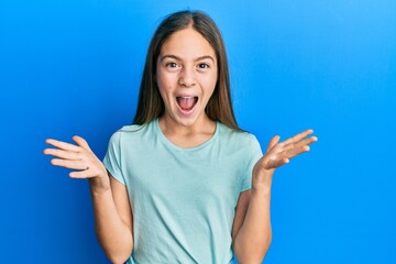 Beautiful brunette little girl wearing casual white t shirt celebrating crazy and amazed for success with arms raised and open eyes screaming excited. winner concept