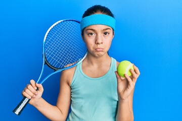 Beautiful brunette little girl playing tennis holding racket and ball depressed and worry for...
