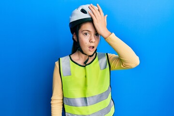 Beautiful brunette little girl wearing bike helmet and reflective vest surprised with hand on head for mistake, remember error. forgot, bad memory concept.