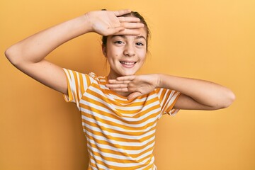 Fototapeta na wymiar Beautiful brunette little girl wearing casual striped t shirt smiling cheerful playing peek a boo with hands showing face. surprised and exited