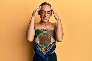 Hispanic man wearing make up and long hair wearing womans top with hand on head for pain in head because stress. suffering migraine.