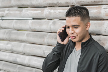 young latino, university student talking on his cell phone with happiness on his face, leaning on a guadua hut, young entrepreneur and influencer with his cell phone in his hand. technological concept