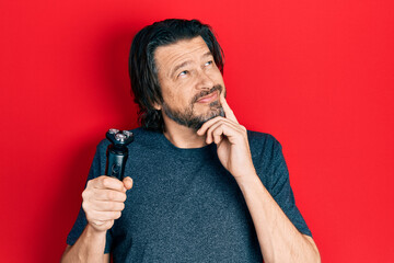 Middle age caucasian man holding electric razor machine serious face thinking about question with...