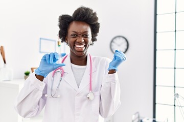 Naklejka premium African doctor woman holding syringe at medical clinic screaming proud, celebrating victory and success very excited with raised arm