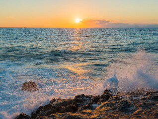 romantic sunset on the mediterranean coast with bursts of sea waves in the sun