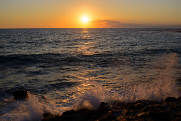 romantic sunset on the mediterranean coast with bursts of sea waves in the sun