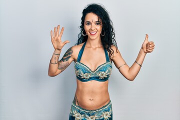 Fototapeta premium Young woman wearing bindi and traditional belly dance clothes showing and pointing up with fingers number six while smiling confident and happy.