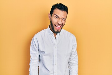 Hispanic man with beard wearing business shirt winking looking at the camera with sexy expression, cheerful and happy face.