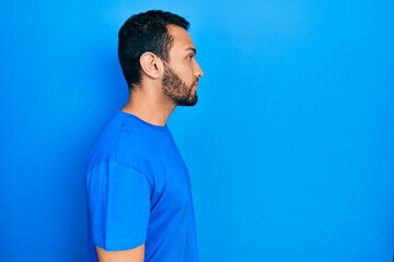 Hispanic man with beard wearing casual blue t shirt looking to side, relax profile pose with natural face with confident smile.