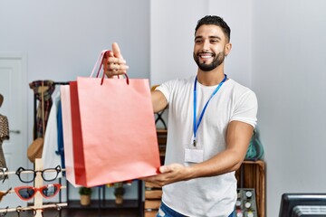 Young arab man shopkeeper holding shopping bags working at clothing store