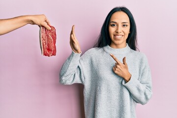 Young hispanic girl on diet rejecting beef smiling happy pointing with hand and finger