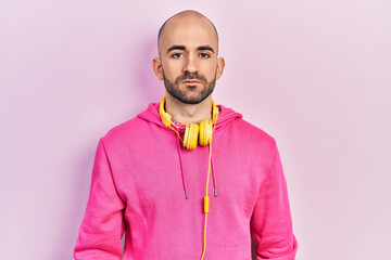 Young bald man wearing gym clothes and using headphones relaxed with serious expression on face. simple and natural looking at the camera.