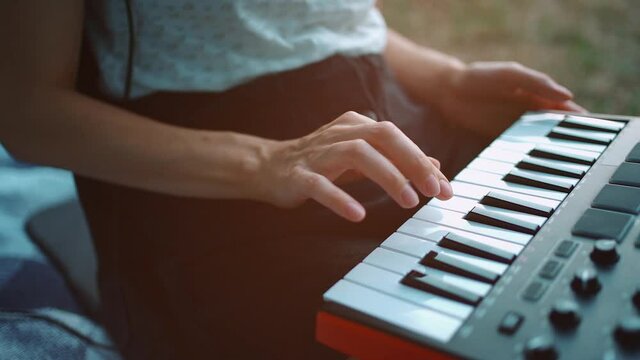 closeup of girl hand playing midi keyboard synthesizer and compose music outdoor