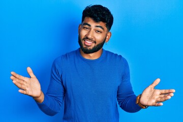 Arab man with beard wearing casual blue sweater clueless and confused expression with arms and hands raised. doubt concept.