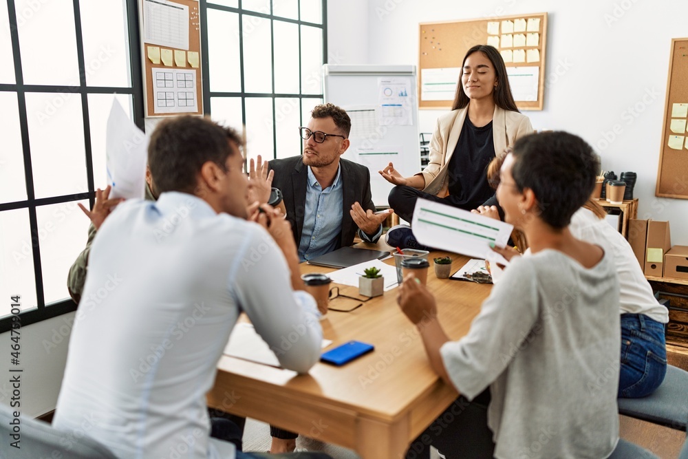 Wall mural Businesswoman enjoys meditating during meeting. Sitting on desk near arguing partners at the office.