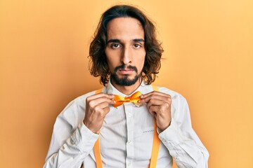 Young hispanic man wearing hipster elegant look holding bowtie relaxed with serious expression on...