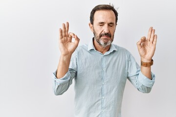 Middle age hispanic man with beard standing over isolated background relaxed and smiling with eyes closed doing meditation gesture with fingers. yoga concept.