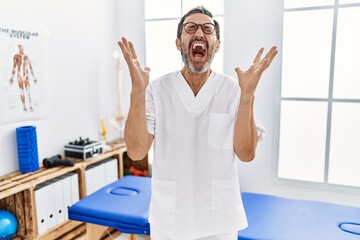 Middle age man with beard working at pain recovery clinic celebrating mad and crazy for success with arms raised and closed eyes screaming excited. winner concept