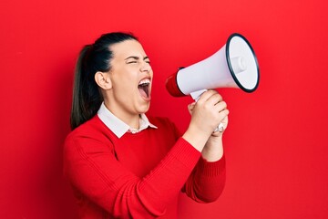 Young brunette woman screaming through megaphone over isolated red background