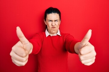 Young hispanic woman doing thumbs up positive gesture skeptic and nervous, frowning upset because of problem. negative person.