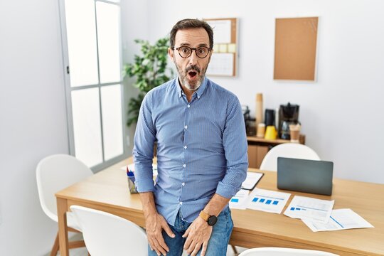 Middle age hispanic man with beard wearing business clothes at the office afraid and shocked with surprise expression, fear and excited face.