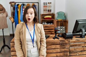 Young down syndrome woman working as manager at retail boutique afraid and shocked with surprise expression, fear and excited face.