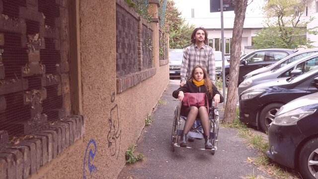 help, assistance - slow motion on young man accompaning his girlfriend using wheelchair for a walk in the city