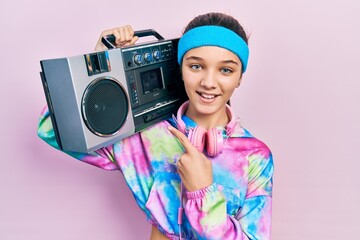 Young brunette girl wearing workout clothes and holding boombox smiling happy pointing with hand and finger