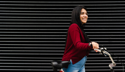 young latin woman with her bicycle in her hand smiling, black background copy space lines