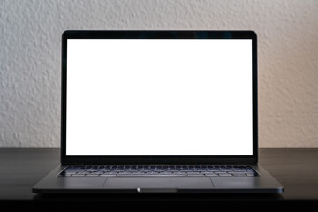 Empty laptop screen perfect for testing and a mockup of a design. Bright white screen in a dark environment. Device standing on a black wooden desk in front of a white wall.